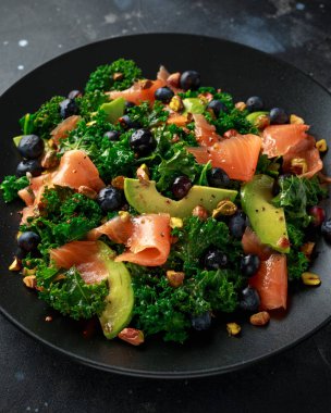 Somon Kale süper yiyecek salata avokado, Antep fıstığı ve siyah plaka üzerinde yaban mersini