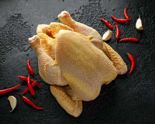 Raw whole chicken with spices on dark background