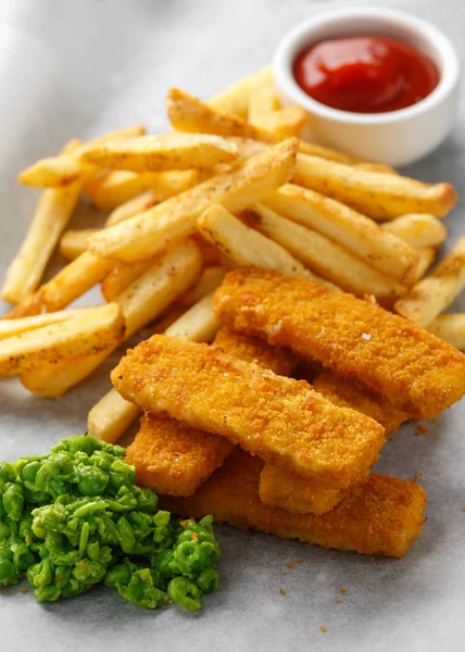 Fiskpinnar, mosade ärtor och chips frites. Traditionella brittiska snabbmat. serveras på skrynkligt papper — Stockfoto