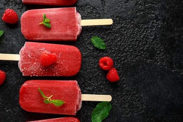 Homemade raspberry popsicles, ice lolly on rustic black background