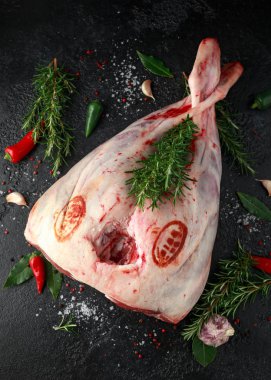 Ham kuzu bacak otlar ile siyah taş tabloda. sarımsak, biberiye, biber, tuz, karabiber, defne yaprağı.