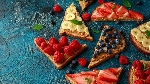 Jordnötssmör smörgåsar med färska jordgubbar, blåbär, hallon och banan hela måltiden skålar. — Stockfoto