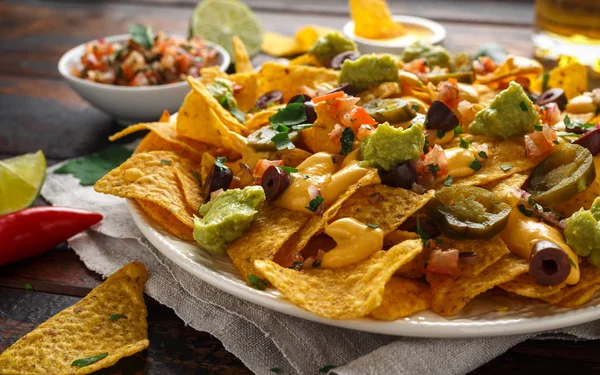 Mexican nachos tortilla chips with olives, jalapeno, guacamole, tomatoes salsa, cheese dipand beer.