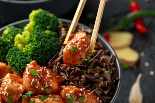 Teriyaki chicken, steamed broccoli and wild rice served in two Asian clay bowls.