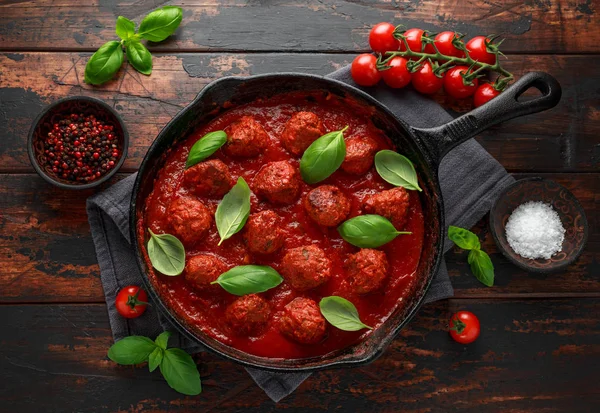 Albóndigas caseras en hierro fundido con salsa de tomate dulce y caliente, albahaca. Sobre mesa de madera — Foto de Stock