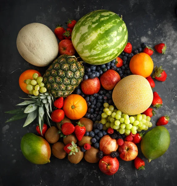 Różnorodność świeżych owoców i jagód na ciemnym tle: Cantaloupe, melon, arbuz, Blueberry, pomarańcze, jabłko, truskawka, ananas, mango, winogrona i kiwi. — Zdjęcie stockowe