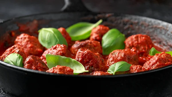 Albóndigas caseras en hierro fundido con salsa de tomate dulce y caliente, albahaca. Sobre mesa de madera — Foto de Stock