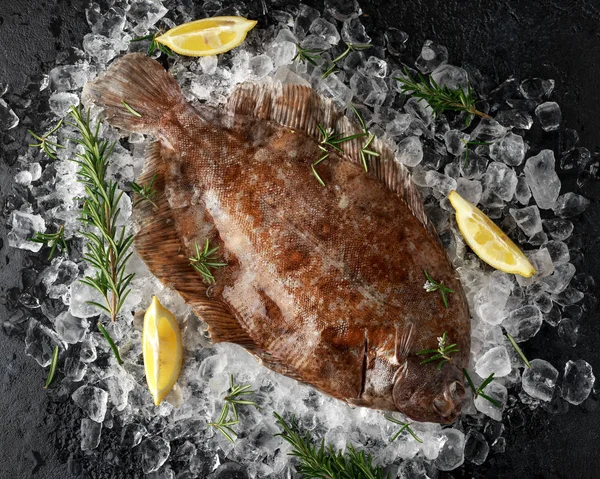 Raw lemon sole fish on ice with herbs and lemon wedges