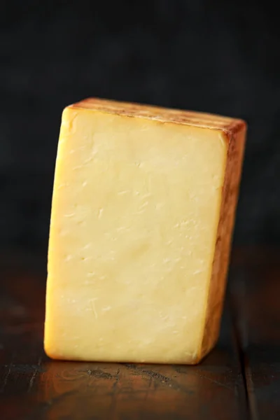 Bitesize Slice of smoked cheddar cheese on rustic wooden background — Stock Photo, Image