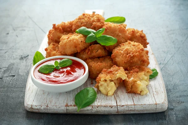 Fried Mac, macaroni and Cheese Bites in breadcrumbs with ketchup sauce on white wooden board