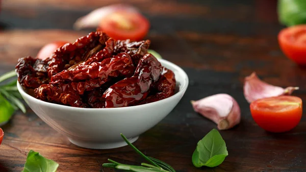 Sonnengetrocknete Tomaten in weißer Schüssel mit frischen Kräutern und Gewürzen auf Holztisch — Stockfoto