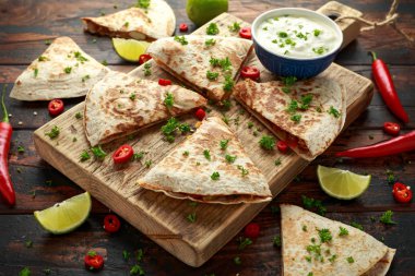 Ahşap tahta üzerinde tavuk, mısır, siyah fasulye, peynir, sebze, kireç ve yoğurt sos ile Meksika quesadilla