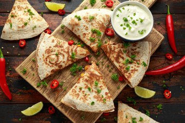 Ahşap tahta üzerinde tavuk, mısır, siyah fasulye, peynir, sebze, kireç ve yoğurt sos ile Meksika quesadilla