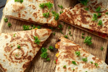Ahşap tahta üzerinde tavuk, mısır, siyah fasulye, peynir, sebze, kireç ve yoğurt sos ile Meksika quesadilla
