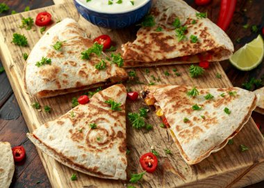 Ahşap tahta üzerinde tavuk, mısır, siyah fasulye, peynir, sebze, kireç ve yoğurt sos ile Meksika quesadilla