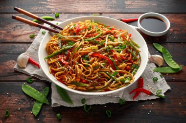 Chow mein, noodles and vegetables dish with wooden chopsticks clipart