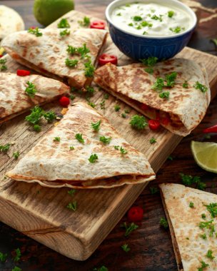 Ahşap tahta üzerinde tavuk, mısır, siyah fasulye, peynir, sebze, kireç ve yoğurt sos ile Meksika quesadilla