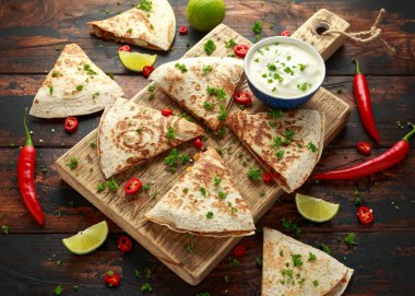 Ahşap tahta üzerinde tavuk, mısır, siyah fasulye, peynir, sebze, kireç ve yoğurt sos ile Meksika quesadilla