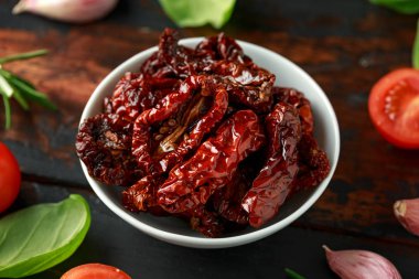 Ahşap masada taze otlar ve baharatlar ile beyaz kapta Güneş kurutulmuş domates