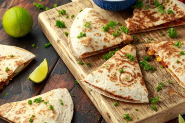 Ahşap tahta üzerinde tavuk, mısır, siyah fasulye, peynir, sebze, kireç ve yoğurt sos ile Meksika quesadilla