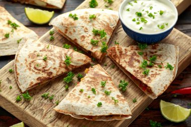 Ahşap tahta üzerinde tavuk, mısır, siyah fasulye, peynir, sebze, kireç ve yoğurt sos ile Meksika quesadilla