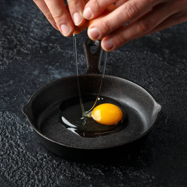 Hans dökme demir kızartma tavası içine yumurta kırma, koyu arka plan üzerinde tava