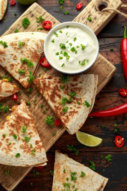 Ahşap tahta üzerinde tavuk, mısır, siyah fasulye, peynir, sebze, kireç ve yoğurt sos ile Meksika quesadilla