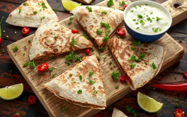 Ahşap tahta üzerinde tavuk, mısır, siyah fasulye, peynir, sebze, kireç ve yoğurt sos ile Meksika quesadilla