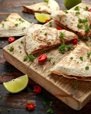 Ahşap tahta üzerinde tavuk, mısır, siyah fasulye, peynir, sebze, kireç ve yoğurt sos ile Meksika quesadilla