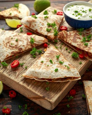 Ahşap tahta üzerinde tavuk, mısır, siyah fasulye, peynir, sebze, kireç ve yoğurt sos ile Meksika quesadilla