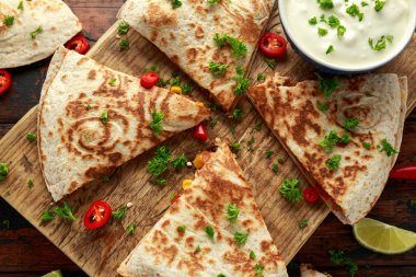 Ahşap tahta üzerinde tavuk, mısır, siyah fasulye, peynir, sebze, kireç ve yoğurt sos ile Meksika quesadilla