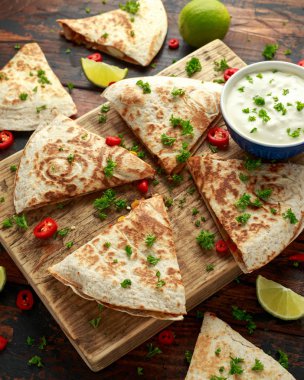 Ahşap tahta üzerinde tavuk, mısır, siyah fasulye, peynir, sebze, kireç ve yoğurt sos ile Meksika quesadilla
