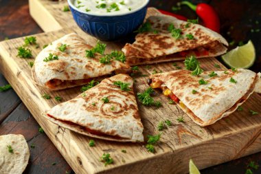 Ahşap tahta üzerinde tavuk, mısır, siyah fasulye, peynir, sebze, kireç ve yoğurt sos ile Meksika quesadilla