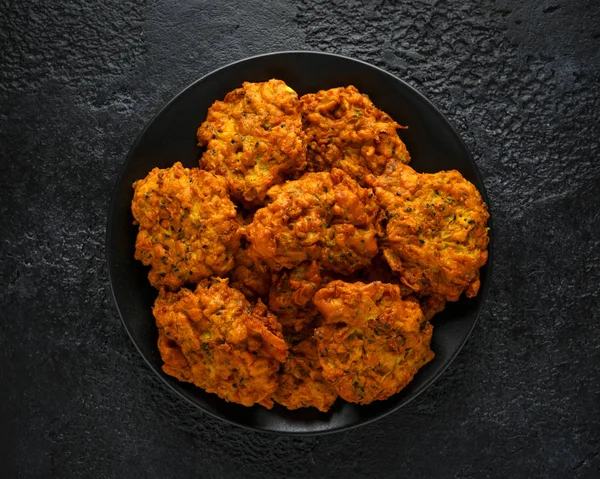 Indian takeaway food, spicy onion bhajis on black plate