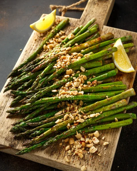 Fried asparagus tips served with crispy crushed peanuts on wooden board — Stock Photo, Image