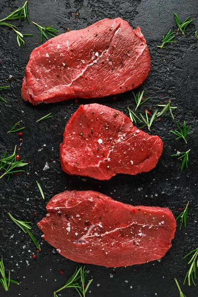 Bife de carne crua crua fresco com ervas em fundo rústico preto — Fotografia de Stock