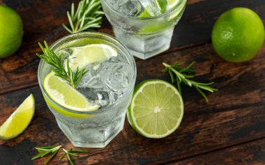 Ahşap masa üzerinde Kireç, Biberiye ve buz ile Cin ve Tonik Alkol içki