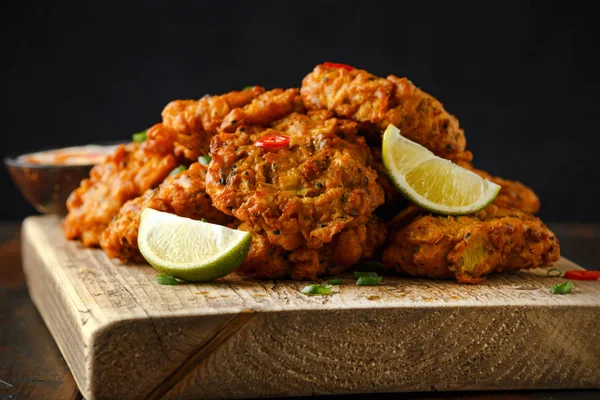 Comida indiana takeaway, bhajis de cebola picante servido com molho de iogurte de pimenta e fatias de limão em tábua de madeira — Fotografia de Stock