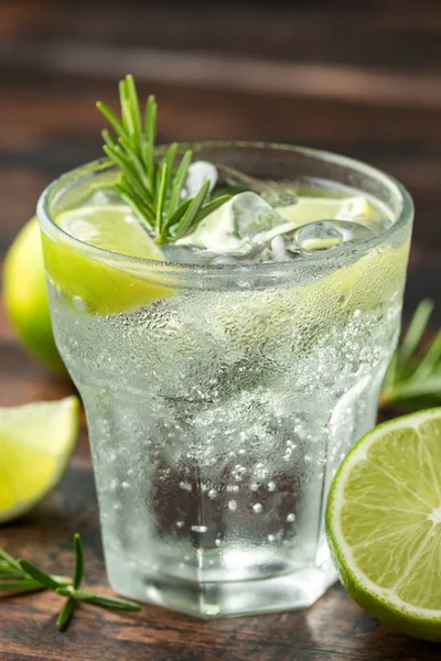 Ahşap masa üzerinde Kireç, Biberiye ve buz ile Cin ve Tonik Alkol içki