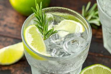 Ahşap masa üzerinde Kireç, Biberiye ve buz ile Cin ve Tonik Alkol içki