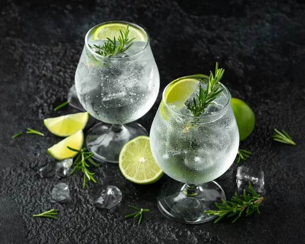 Gin i tonik alkohol pić z limonka, rozmaryn i lód na rustykalny czarny stół — Zdjęcie stockowe