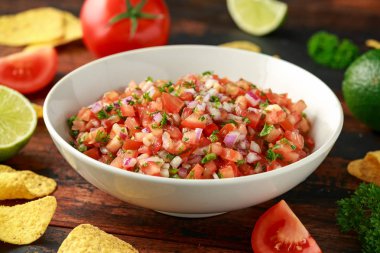 Limon, kırmızı soğan, jalapeno biber, maydanoz ve ahşap masada tortilla cips ile beyaz kapta Meksika Domates Salsa