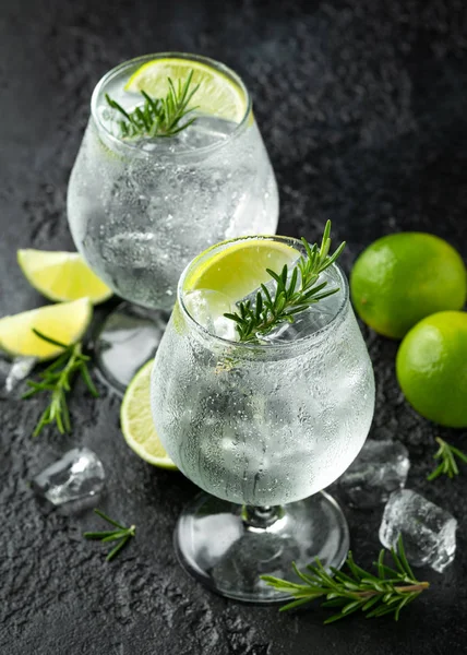 Gin and Tonic Bevanda alcolica con calce, rosmarino e ghiaccio sul tavolo nero rustico — Foto Stock