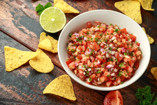 Limon, kırmızı soğan, jalapeno biber, maydanoz ve ahşap masada tortilla cips ile beyaz kapta Meksika Domates Salsa