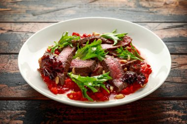 Romesco soslu biftek, beyaz tabakta fındık ve sebze.