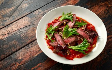 Romesco soslu biftek, beyaz tabakta fındık ve sebze.