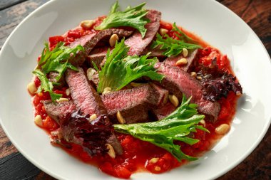 Romesco soslu biftek, beyaz tabakta fındık ve sebze.