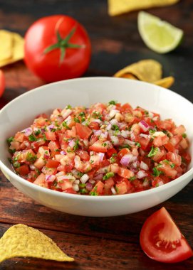 Limon, kırmızı soğan, jalapeno biber, maydanoz ve ahşap masada tortilla cips ile beyaz kapta Meksika Domates Salsa