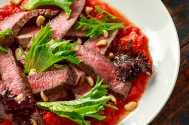 Romesco soslu biftek, beyaz tabakta fındık ve sebze.