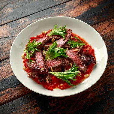 Romesco soslu biftek, beyaz tabakta fındık ve sebze.